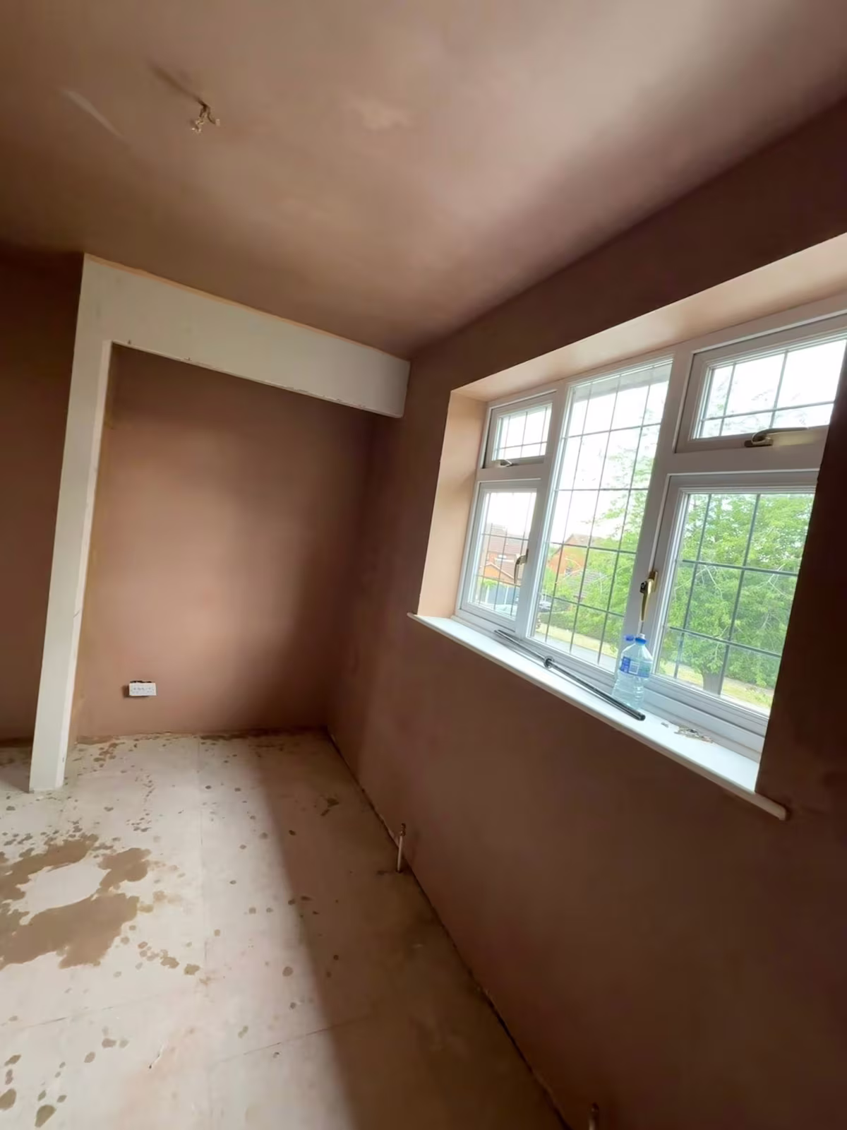 A freshly plastered bedroom with a boxed-in corner and a wide leaded window