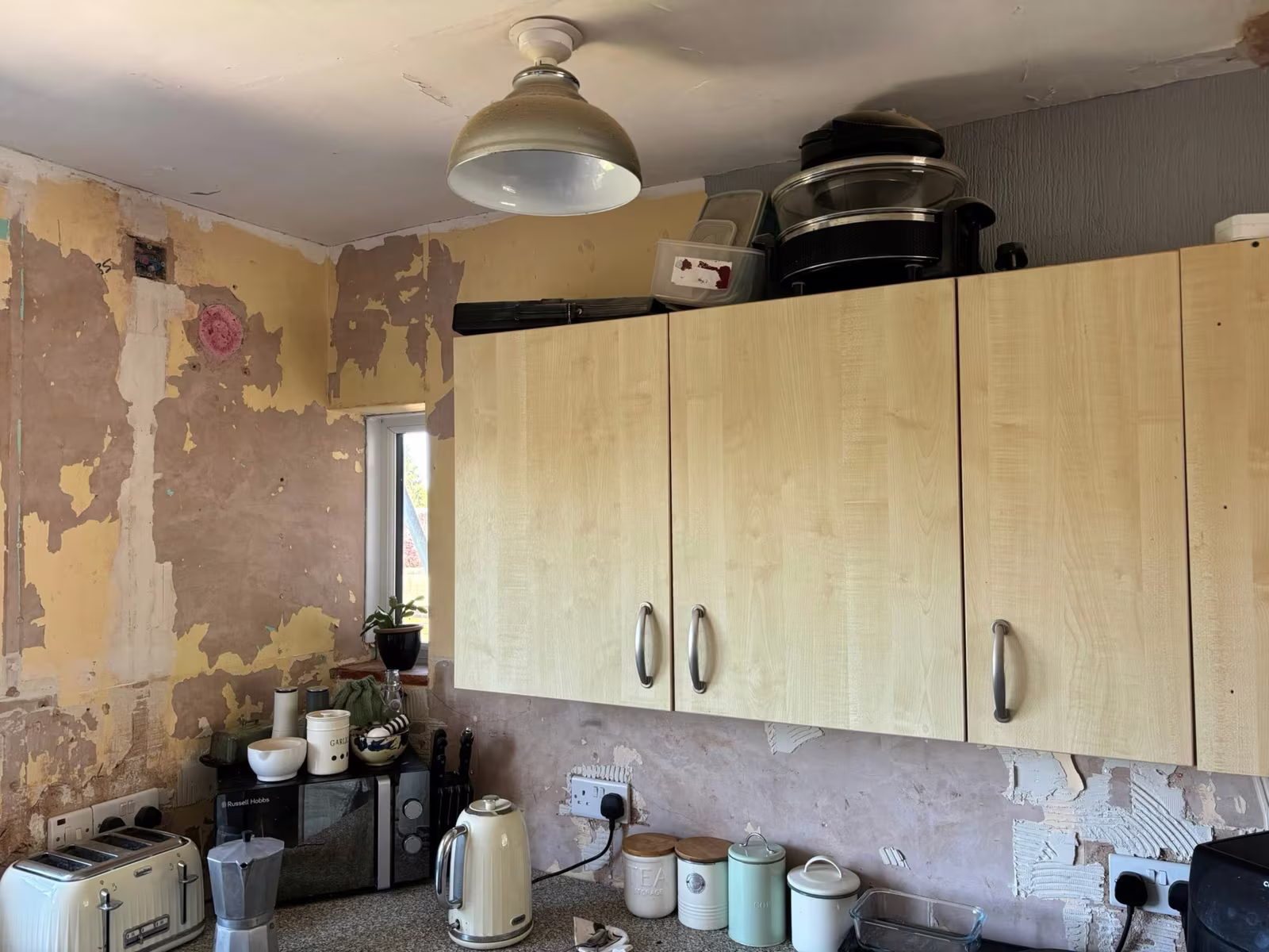 Kitchen walls before plastering, with old wallpaper and plaster stripped back behind the units