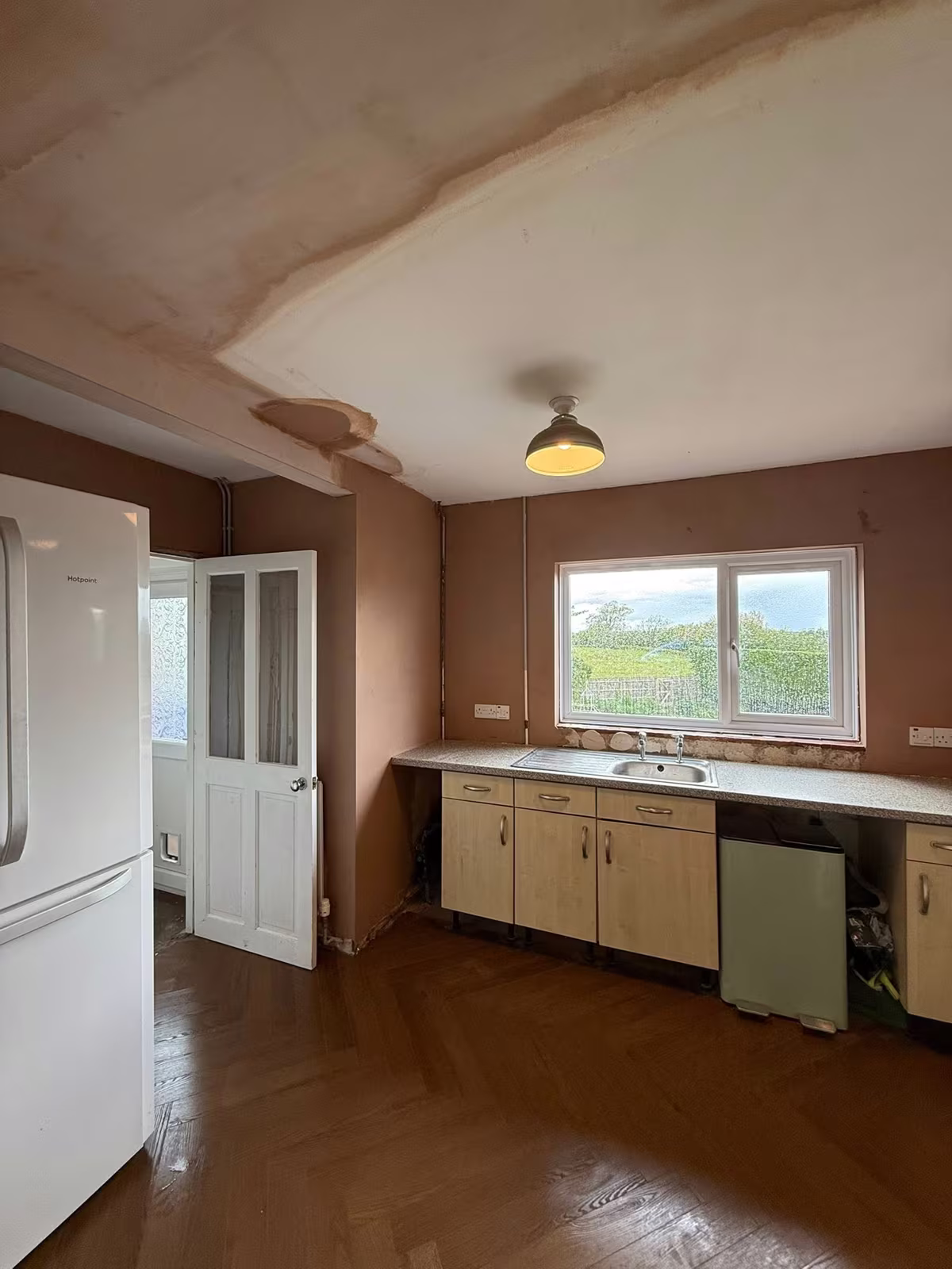 The same kitchen from the doorway, new plaster drying around the fridge and sink