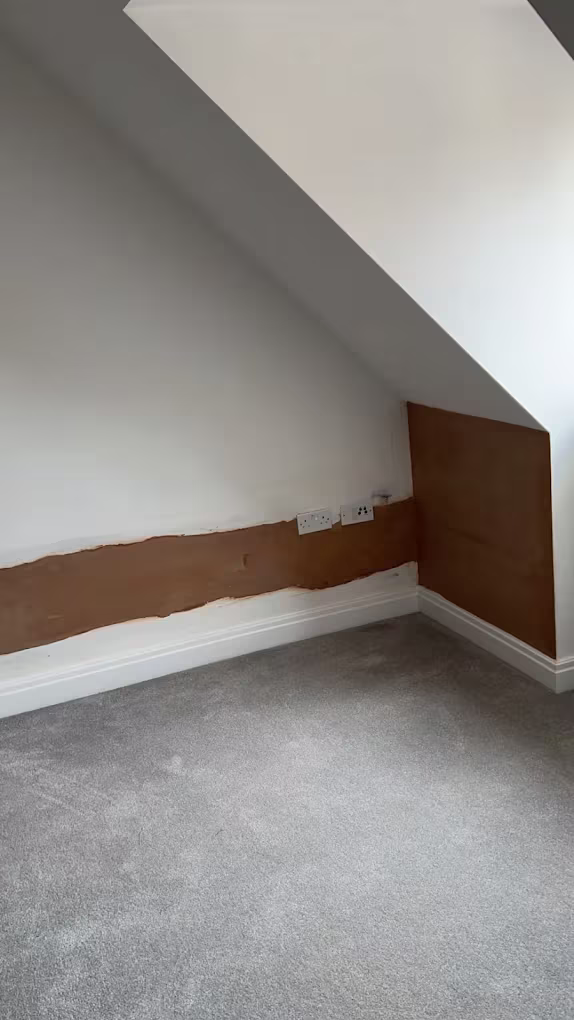 A loft bedroom under a sloping ceiling, with new plaster along the base of the wall