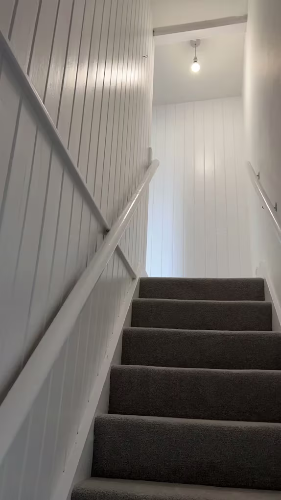 A finished stairwell with painted panelling, handrail and new grey carpet